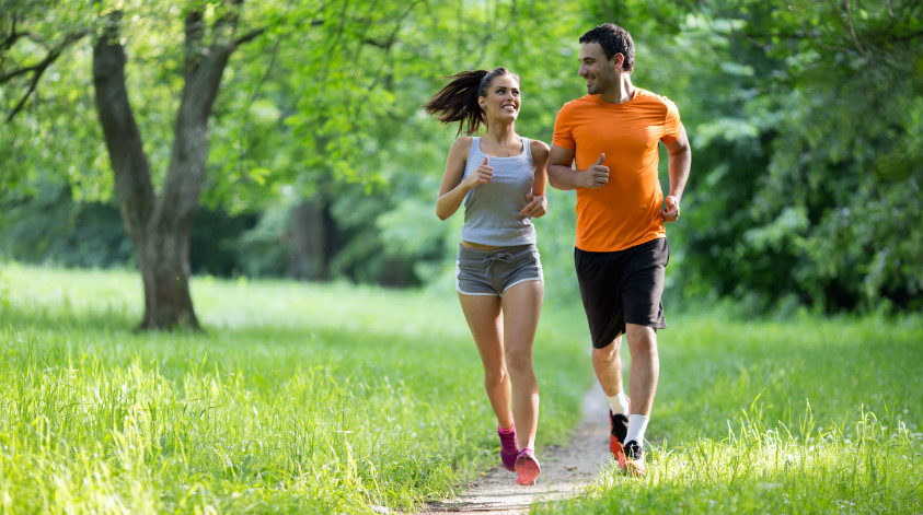 Ein junges Paar joggt in der Natur mit Bäumen im Hintergrund